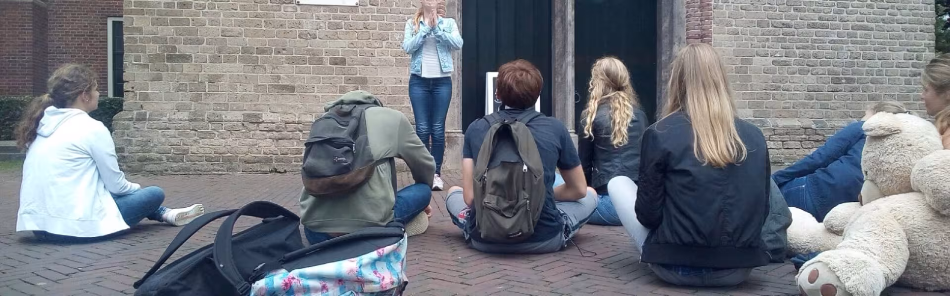 Deelnemers zitten met bagage tegen de muur van het gebouw