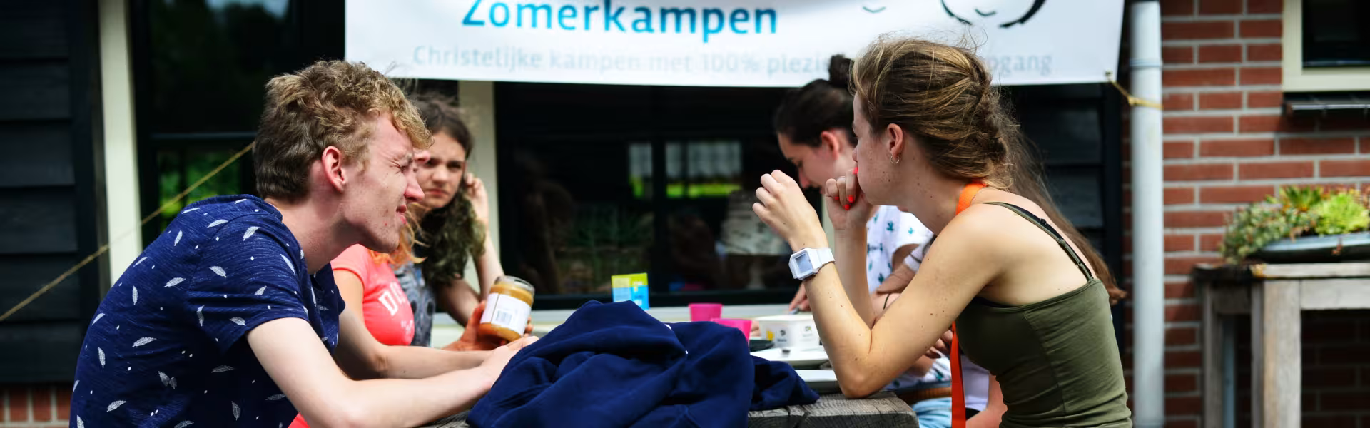 Deelnemers aan een picknicktafel bij het kampgebouw