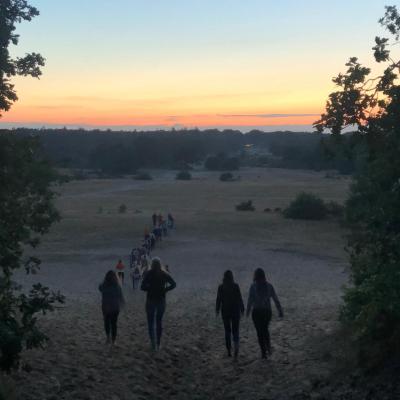 Deelnemers lopen over de heide bij zonsondergang
