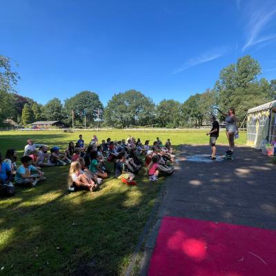 Deelnemers zitten in het gras bij het gebouw