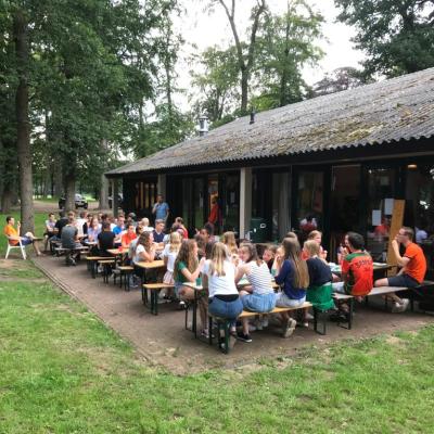 Deelnemers aan picknicktafels bij het kampgebouw