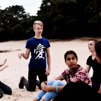 Deelnemers zitten samen in het zand bij avondlicht